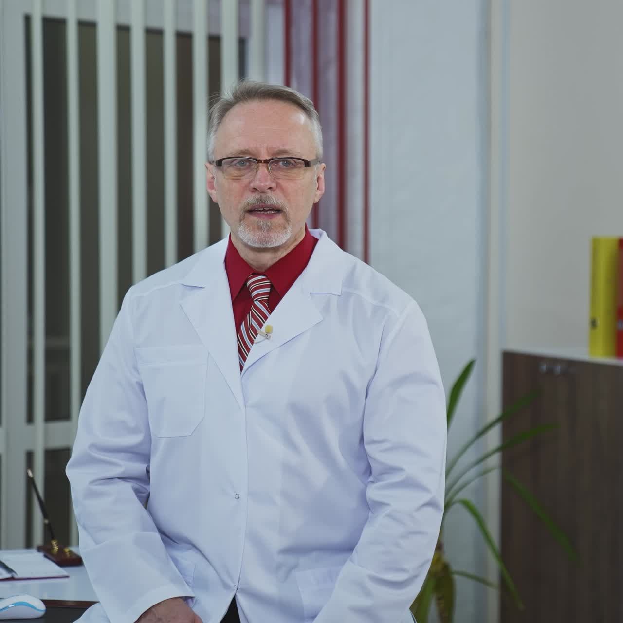 Médico sênior sentado à mesa do consultório e olhando o telefone. Médico experiente e pensativo consulta paciente via videochamada.