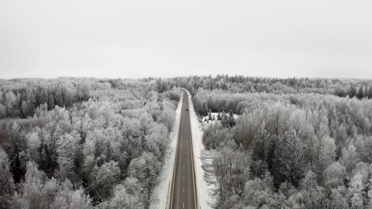 Aerial drone view of a two lane highway through a frozen winter landscape with icy trees and snow covered ground. Hoar frost on trees in countryside.