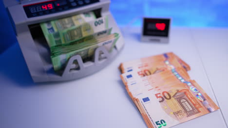 orange fifty euro bills are on the desk. one hundred euro banknotes appear form cash counting machine and female hand puts them on the desk. close up.