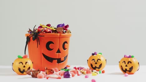 scary halloween pumpkin printed bucket full of candies against grey background