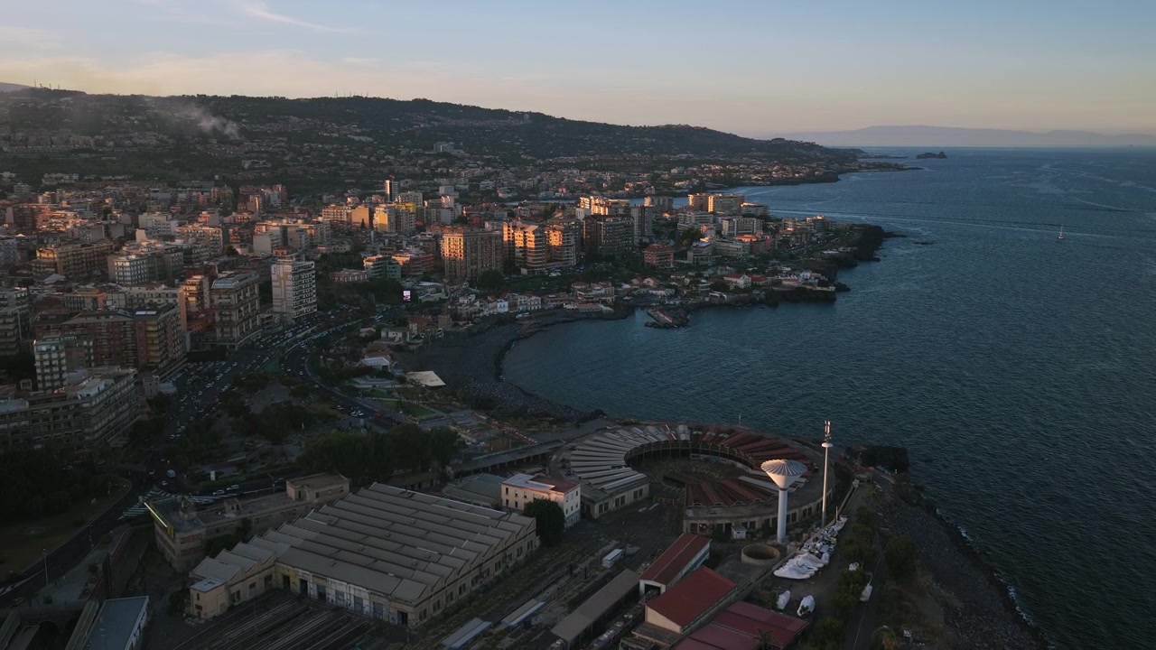 Italia Sicilia. Ripresa aerea con dolly-in di Catania, paesaggio urbano costiero e deposito ferroviario circolare.