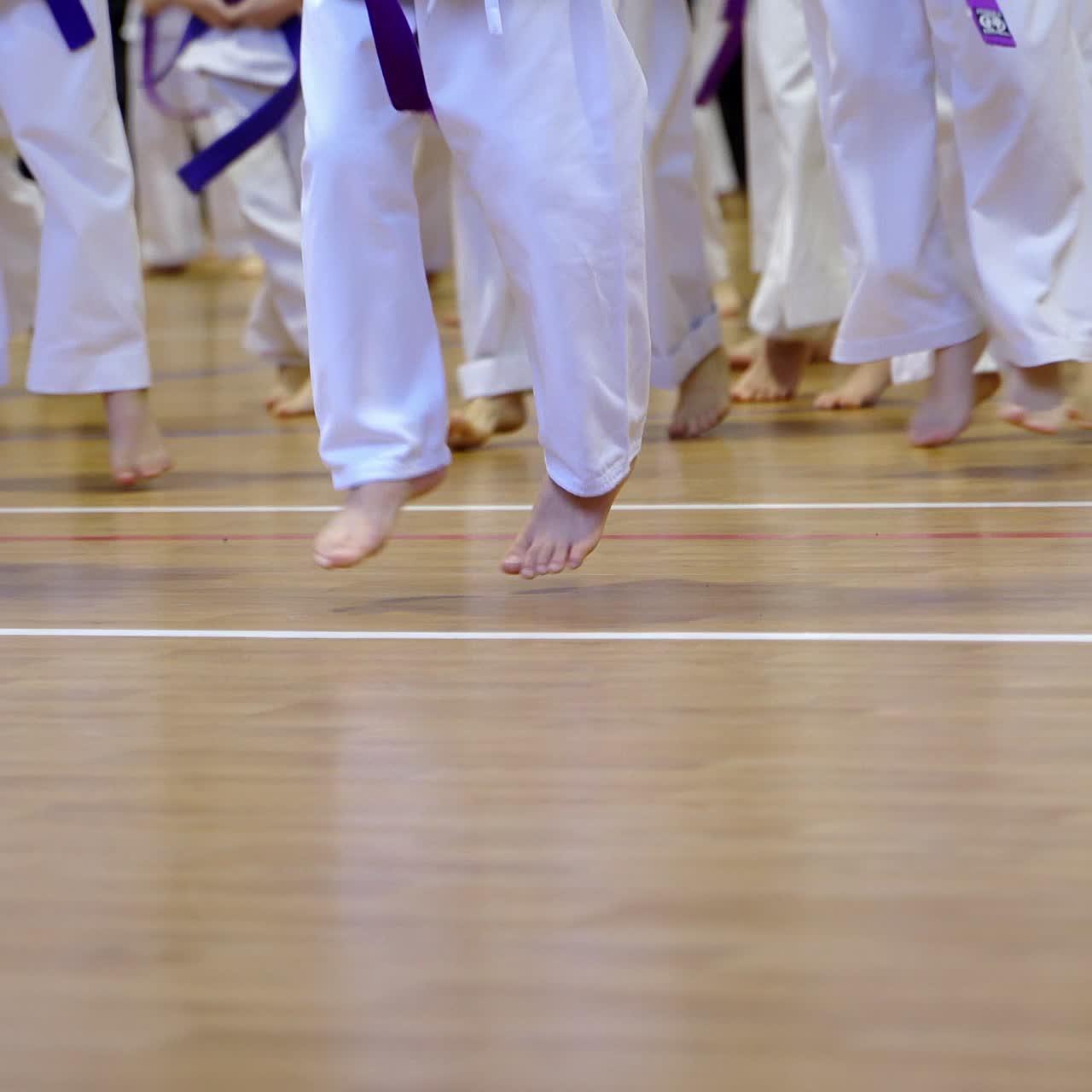 Little sportsmen's bare feet jump on the wooden floor. Athletes in white kimonos warming-up