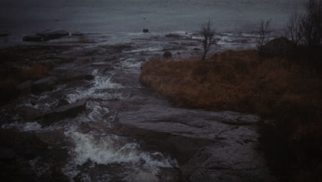 roaring foamy water of fast flowing river meeting sea on rainy and foggy day, lofoten, norway