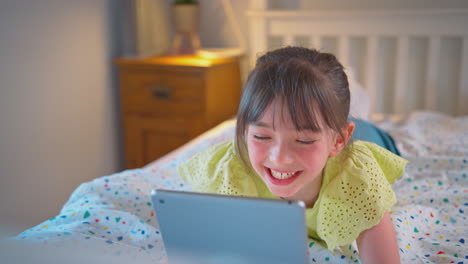 girl in bedroom at home lying on bed using digital tablet