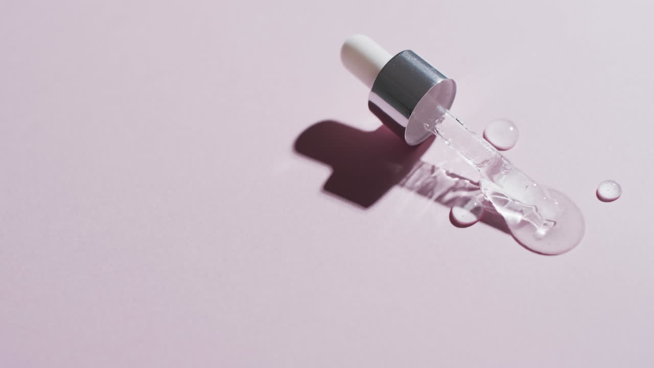 Video of make up pipette and drops of serum with copy space on pink background