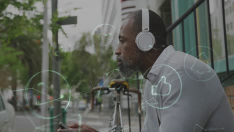 animation of digital icons over man with headphones and smartphone sitting in city street