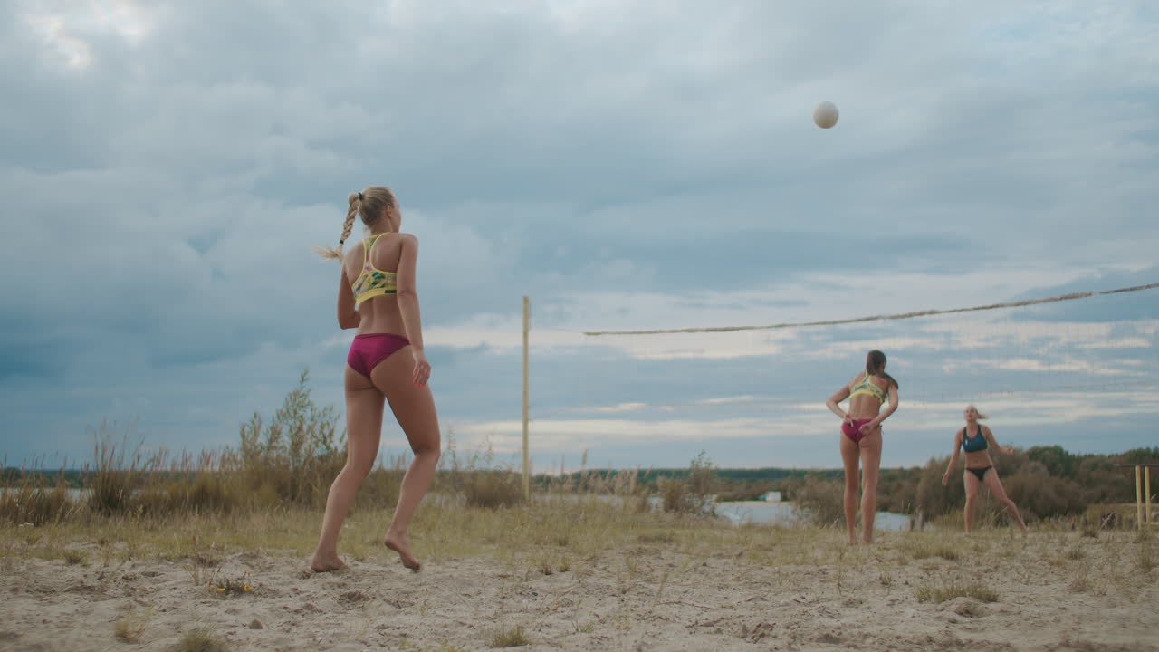 젊은 여성들이 여름 올림픽 스포츠 훈련에서 모래 해변에서 배구 경기를 하고 챔피언십을 준비하고 있습니다.