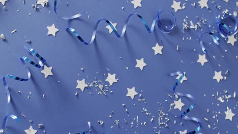 Video-of-multiple-silver-stars-and-party-streamers-scattered-on-blue-background