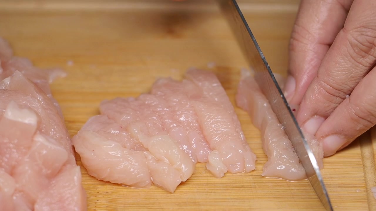 Persona che affetta pollo crudo su un tagliere di legno