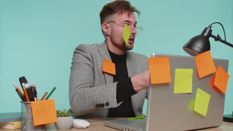 tired exhausted business man at office desk with many tasks stickers, feels sad boredom overworked