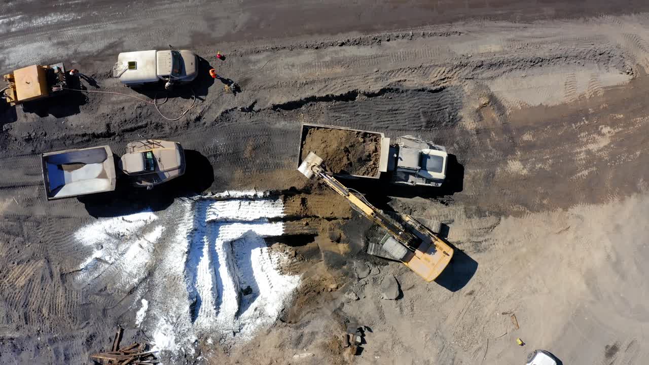 Top down aerial view of an excavator filling up a industrial dump truck, then the truck drives away, static shot