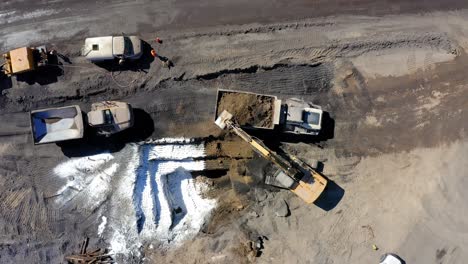 top down aerial view of an excavator filling up a industrial dump truck, then the truck drives away, static shot