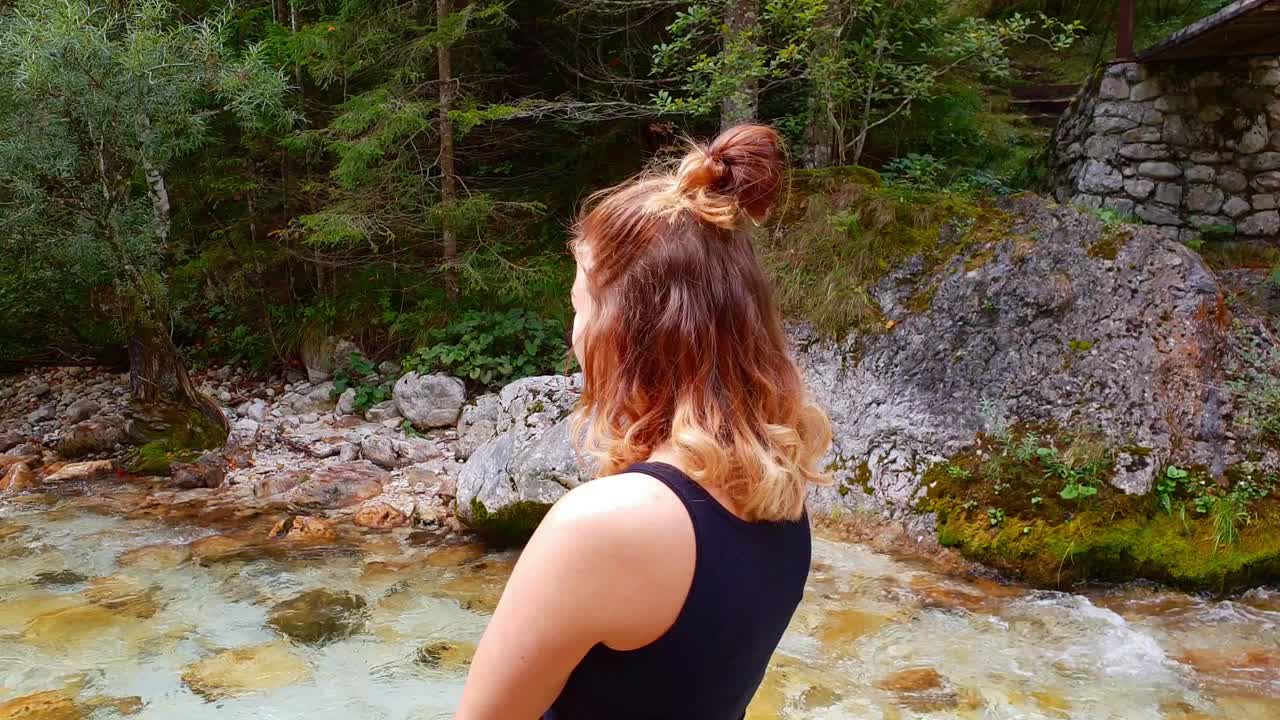 Woman at rapids, shot around a girl standing and looking at the turquoise river, in Trigolov national park, on a sunny summer day, in the Julian alps, Slovenia