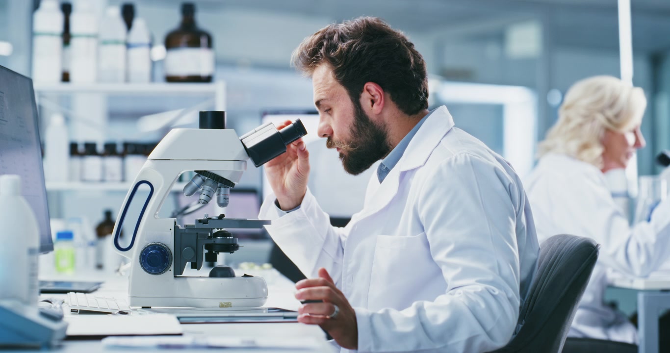 Male Scientist Using Microscope and Tablet in Modern Laboratory