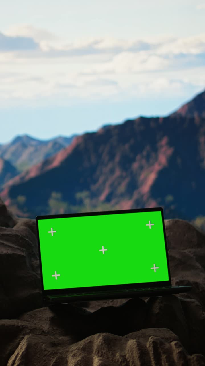 Laptop con display a schermo verde su un paesaggio montano roccioso