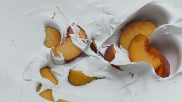 Natural yogurt pieces peach background close up. Fruit falling on creamy dessert
