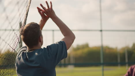 back view of man playing volleyball with lady slamming ball on net in foreground, lady slightly blurred in background, action-focused outdoor volleyball match under bright sky