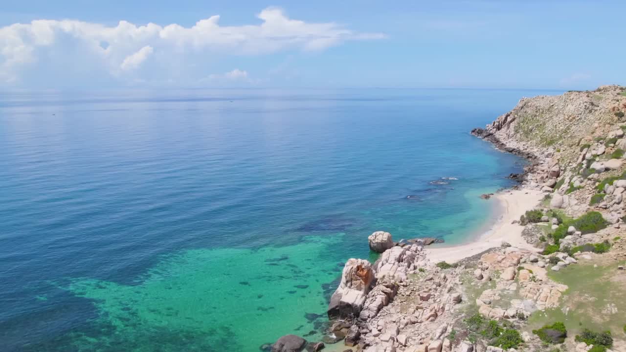 Aerial view of a secluded rocky coastline with turquoise waters and a narrow sandy beach under a bright blue sky