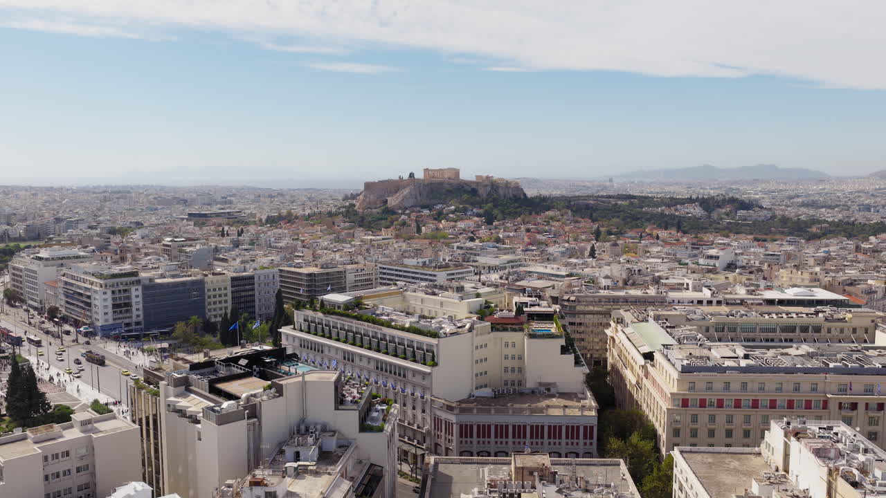 Lenta ripresa panoramica con drone dell'Hotel Grande Bretagne in Piazza Syntagma, con l'Acropoli e il Partenone visibili sullo sfondo in una giornata limpida