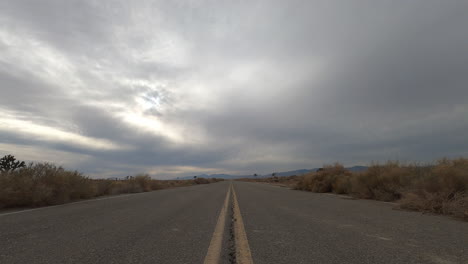 looking down an empty road in the mojave desert with a stormy cloudscape overhead - low angle sunset time lapse