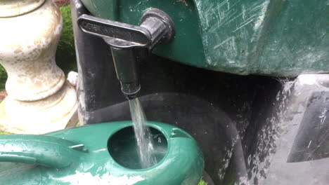 close up of a watering can being filled up from a water butt tap