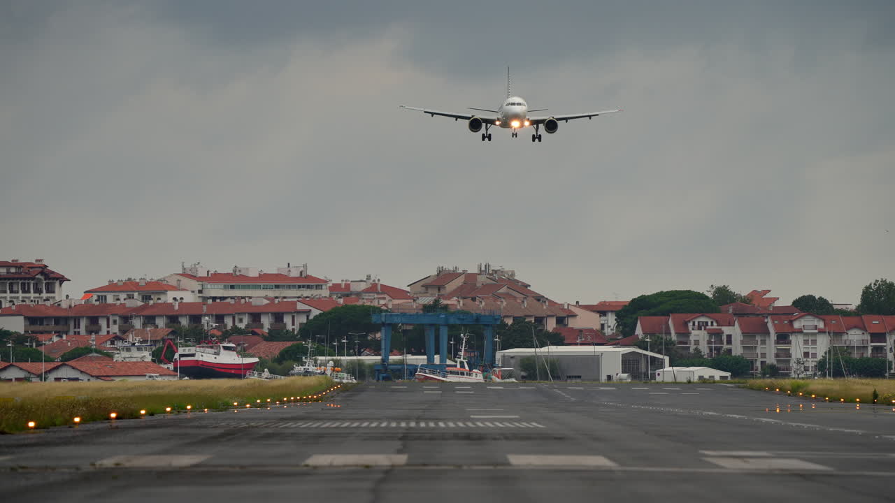 Airplane approaches runway for landing, surrounded by residential buildings and a cloudy sky, showcasing aviation and urban life