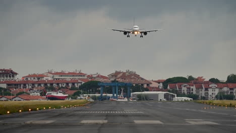 airplane approaches runway for landing, surrounded by residential buildings and a cloudy sky, showcasing aviation and urban life