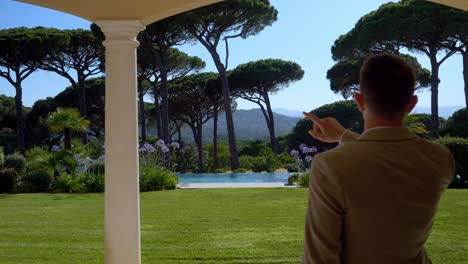 dolly forward shot businessman showing own luxury garden with swimming pools and pine trees