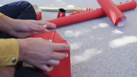 midsection of biracial woman sitting on floor packing christmas presents, slow motion