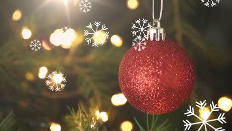 Snowflakes-falling-over-red-bauble-hanging-decoration-against-spot-of-lights