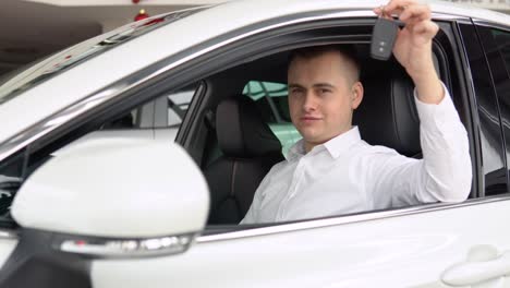 Happy stylish man showing keys of his new car in dealership. Auto business, car sale