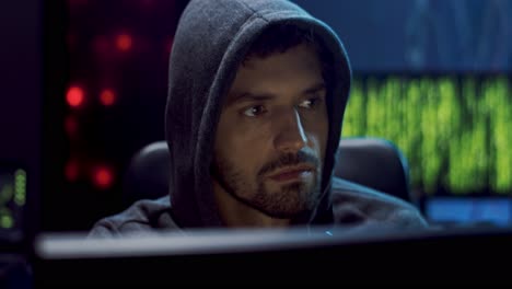 close up of the young male virtual spy in a hood hacking some software at night in the dark room