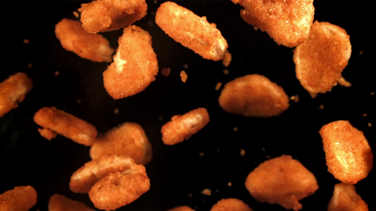 Krispiga gyllene kycklingnuggets som faller i slow motion mot svart bakgrund
