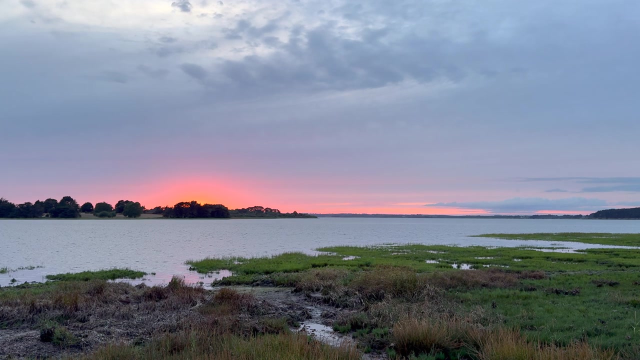 Luce nuvolosa del tramonto su una palude salmastra costiera con erba selvatica e acqua calma in una riserva di zone umide