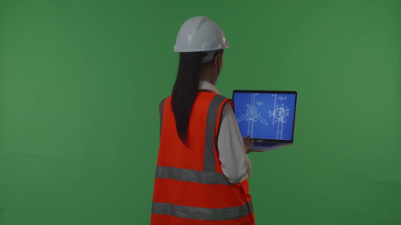 안전 헬을 입은 아시아 여성 엔지니어가 노트북에서 풍력 터빈 블루프린트를 보고 녹색 스크린 배경 스튜디오에 서있는 동안 주위를 둘러보고 있습니다.
