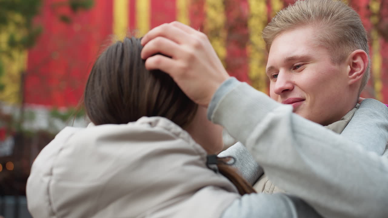 Back view of girl gazing at boyfriend as they look into each other eyes with affection outdoors, man gently adjusting her hair while sharing intimate moment with colorful autumn background