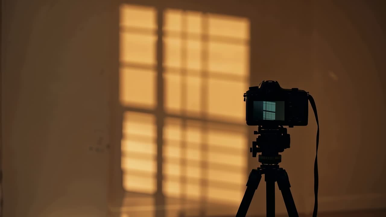 三脚に据えられたデジタル一眼レフカメラが写っており、その背面液晶には日光が部屋の壁に格子状の影を移動させている様子が映し出されている。余白あり。