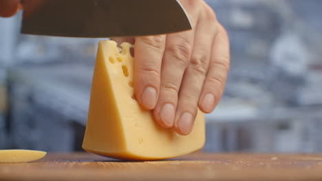 corta el queso amarillo en un tablero de madera de cerca.