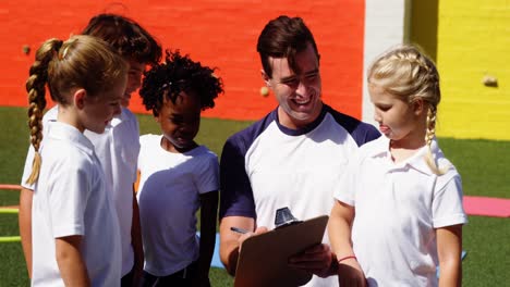 Coach-writing-on-clipboard-while-interacting-with-kids