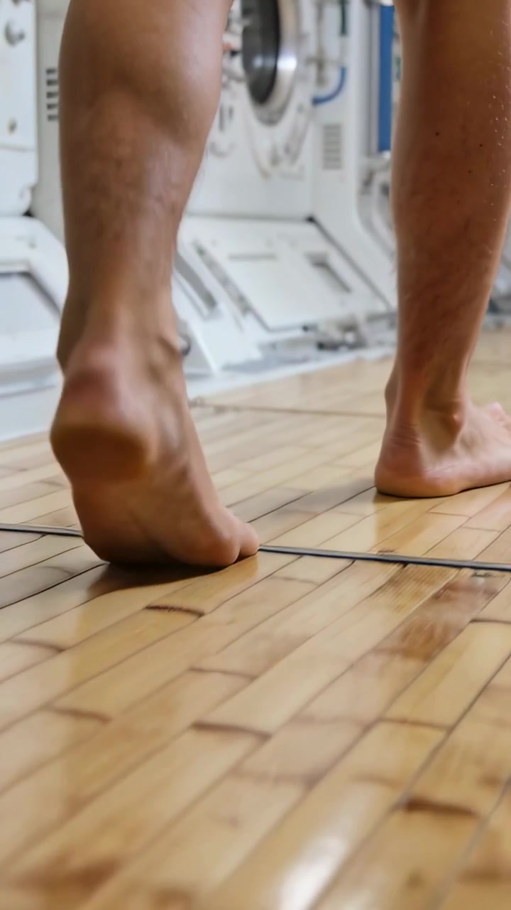 Vertical video: Low shot starting, barefoot man walking heel-toe across module, showing shiny floor