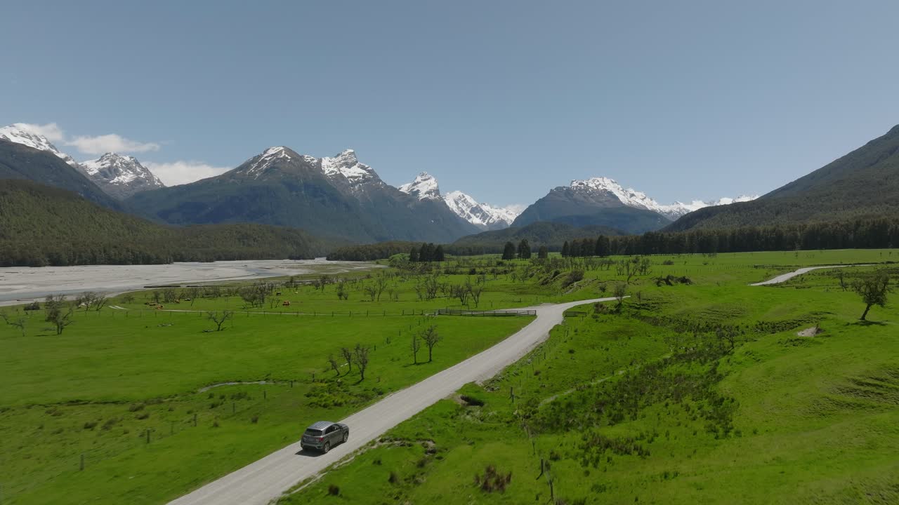 자동차는 눈 덮인 산으로 둘러싸인 뉴질랜드 시골을 여행합니다.