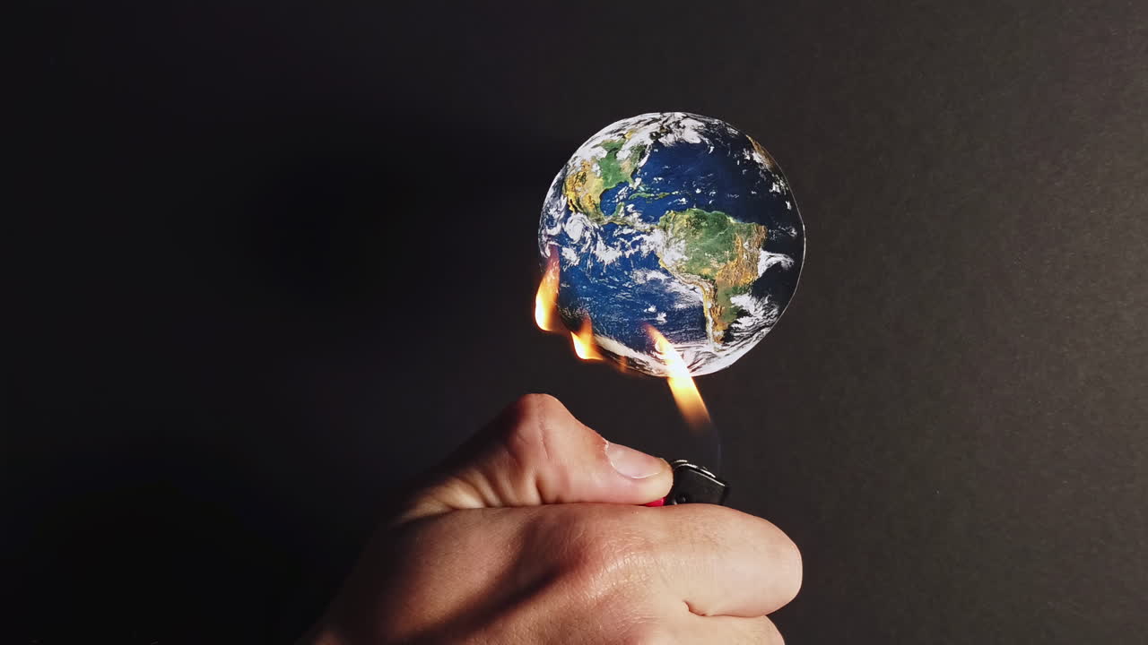 Man hand burns with a lighter the planet earth in front of a black background. Ecology idea. Rapid climate change. Close up. Slow motion