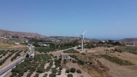 Coches-Que-Viajan-Por-La-Carretera-Rural-Rodeada-Por-Los-Verdes-Olivares-Cerca-Del-Parque-Eólico---Aerogenerador-En-Agrigento,-Sicilia,-Italia