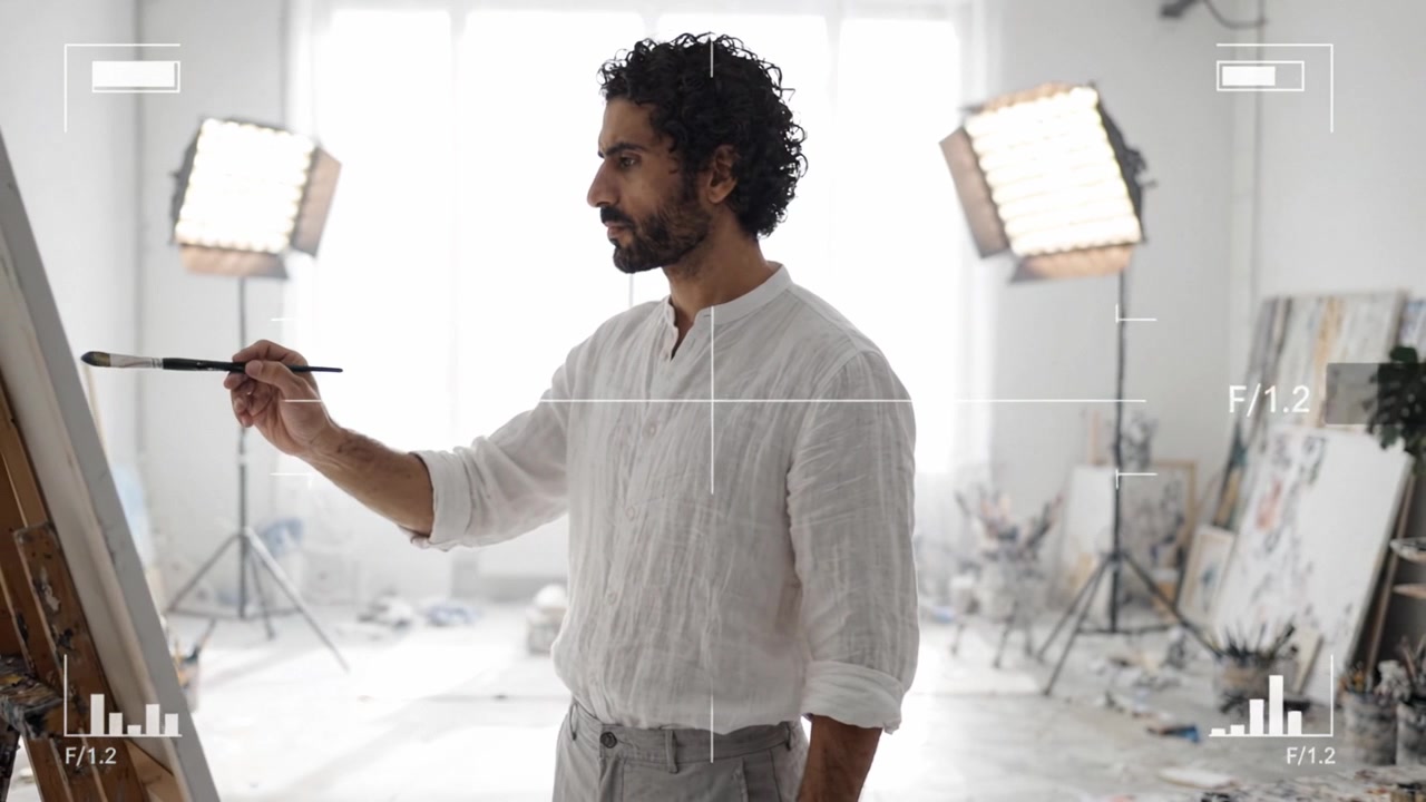 Um Artista em Ação: Momentos Criativos Capturados no Estúdio enquanto um Pintor se Concentra em Sua Tela, Cercado por Arte e Iluminação Brilhante de Estúdio