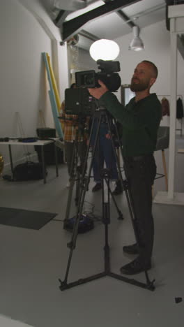 vídeo vertical de un operador de cámara de película masculino grabando una película o un vídeo en un estudio utilizando un trípode 1