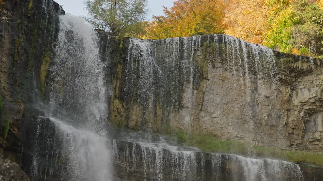 Majestic waterfall cascades over rocky cliffs surrounded by autumn trees in a peaceful setting