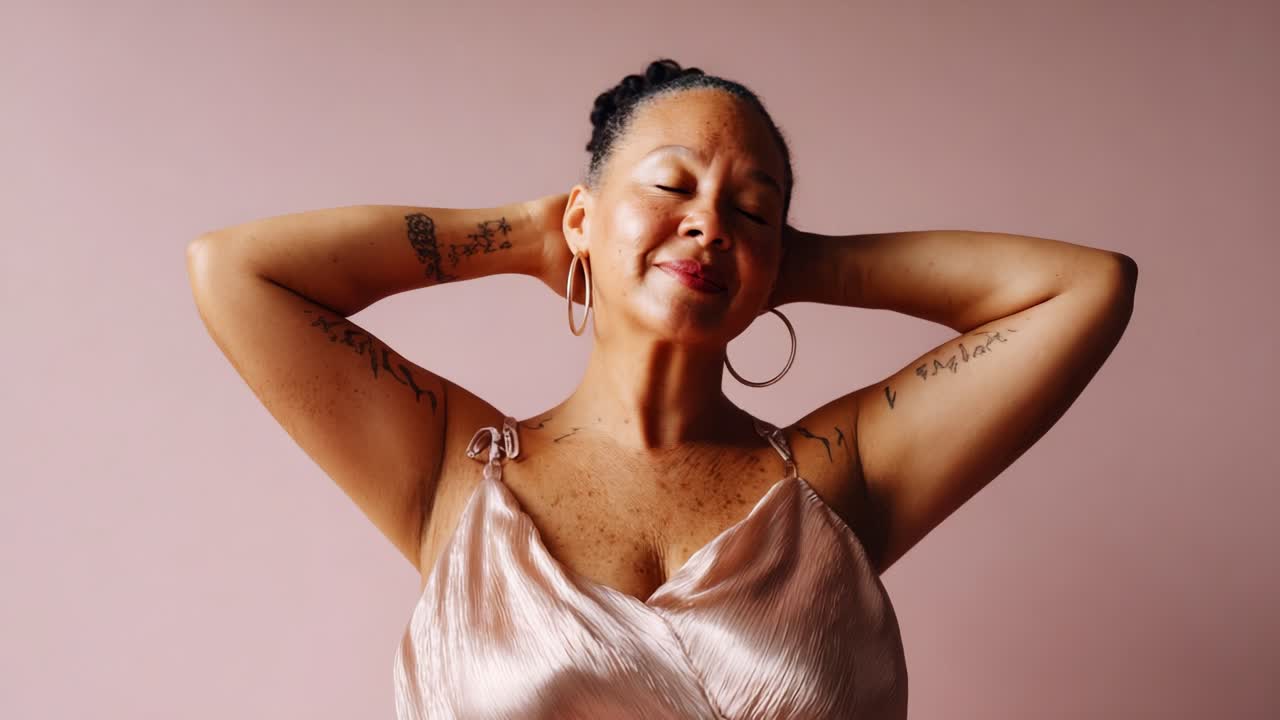 Celebrating Self-Love: A Woman Poses Gracefully with Joy and Confidence, Embracing Her Beauty and Strength Against a Soft Pink Background in a Flowing Satin Top