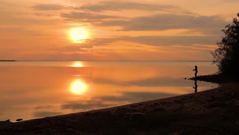 Frau-Fischt-Auf-Angelrute,-Die-Sich-Bei-Sonnenuntergang-Im-Hintergrund-Dreht.