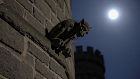 gargoyle on a stone wall at night under a full moon