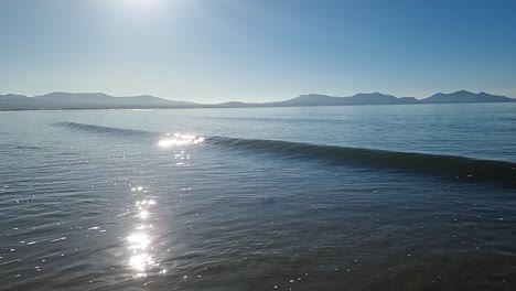 Slow-motion-tide-waves-splashing-under-hazy-sunrise-Snowdonia-mountain-range-skyline